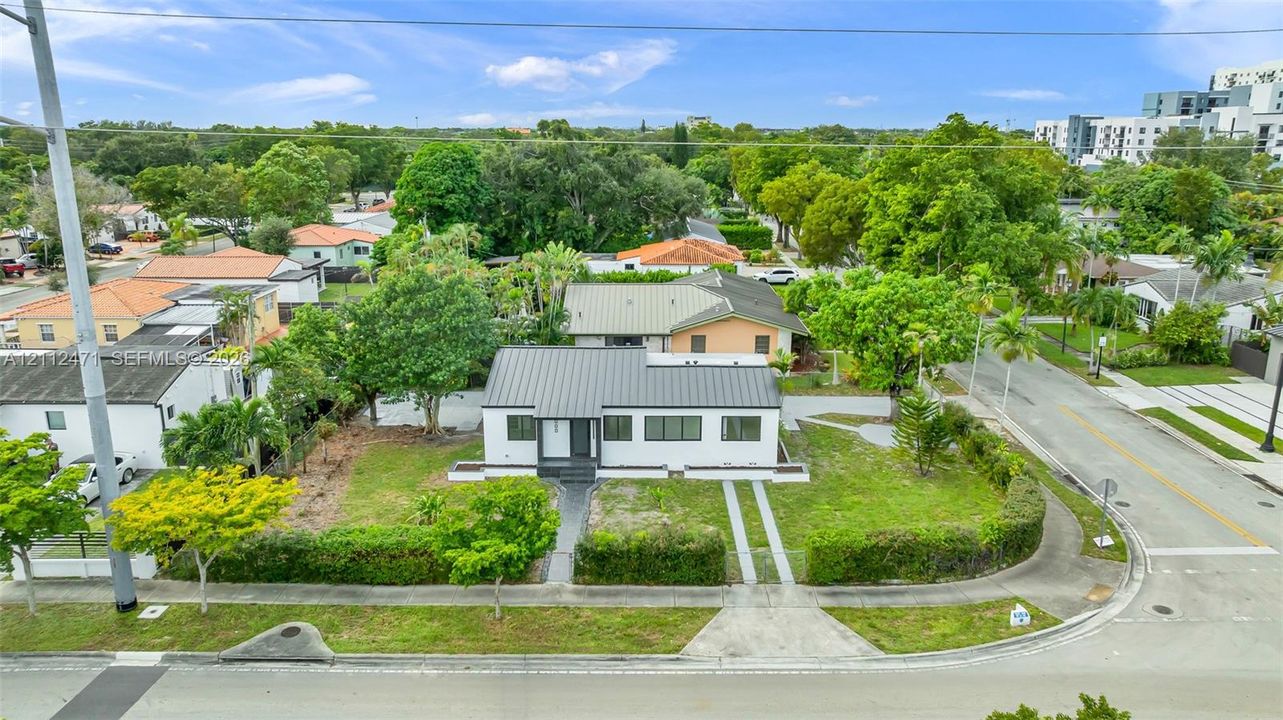 Single-story residence featuring a standing-seam metal roof, white stucco exterior, dark-trimmed windows, a paved walkway, and a landscaped corner lot