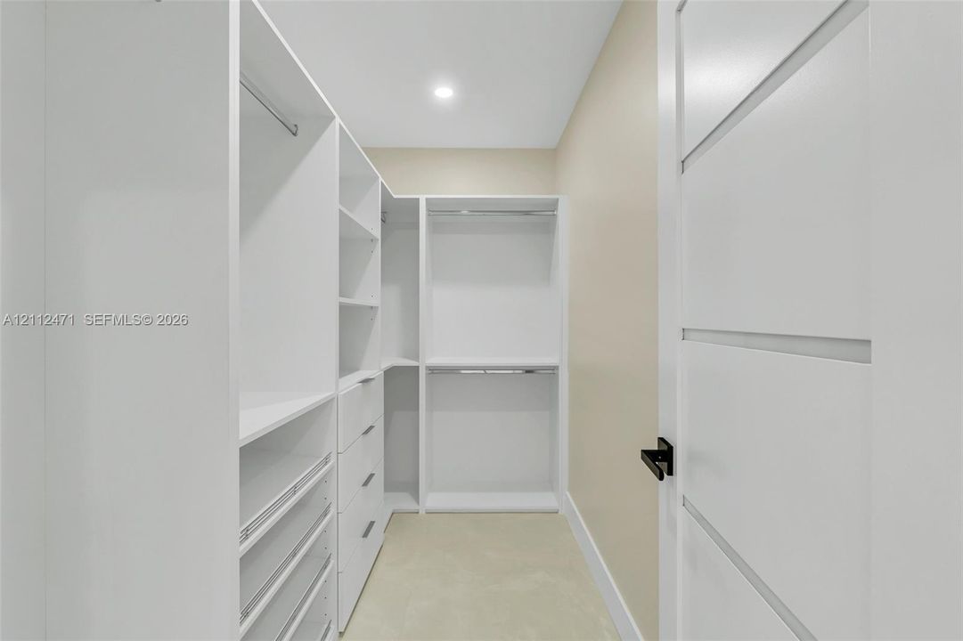 Custom walk-in closet featuring white built-in shelving, integrated dresser drawers, chrome hanging rods, and a multi-panel door with matte black hardware