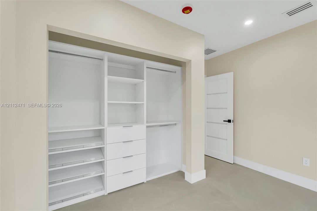 Custom white built-in cabinetry featuring tiered shelving, integrated storage drawers, and hanging rods, complemented by a five-panel interior door with matte black hardware