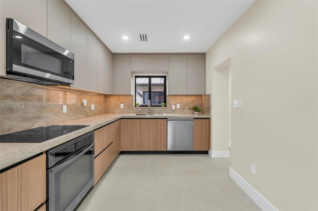 Kitchen featuring flat-panel wood-grain cabinetry, stone-surface countertops, full-height stone-surface backsplash, stainless steel appliances, and recessed lighting