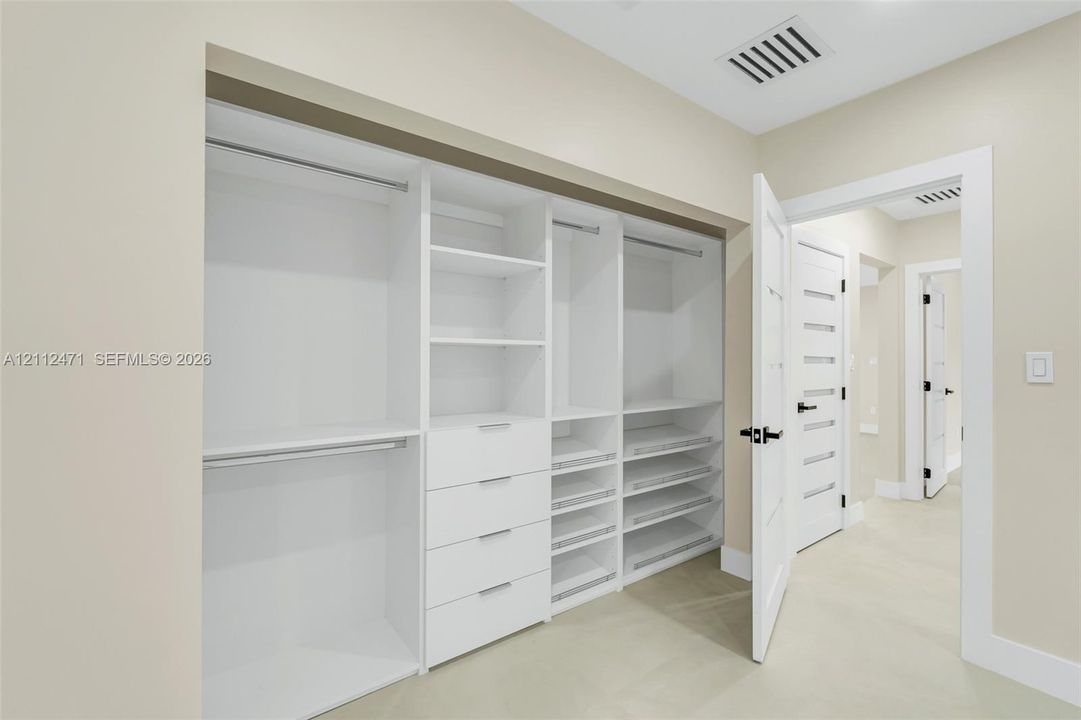 Custom built-in closet featuring floor-to-ceiling white shelving, integrated drawers, pull-out storage racks, and dual hanging rods