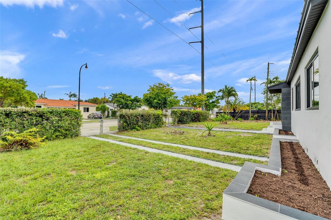 Side yard featuring manicured perimeter hedging, dual concrete paved paths, and multi-level masonry planter beds with dark tile capping