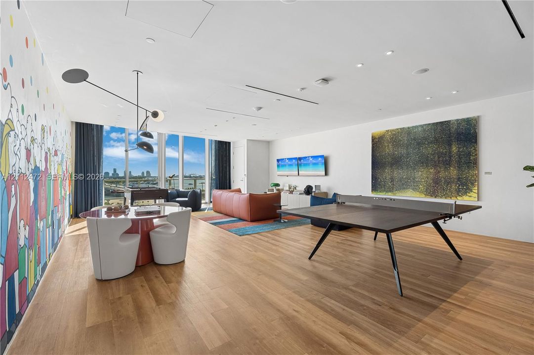 Open-concept living space featuring wood-finish flooring, floor-to-ceiling glass windows, recessed ceiling lighting, and a prominent decorative wall mural