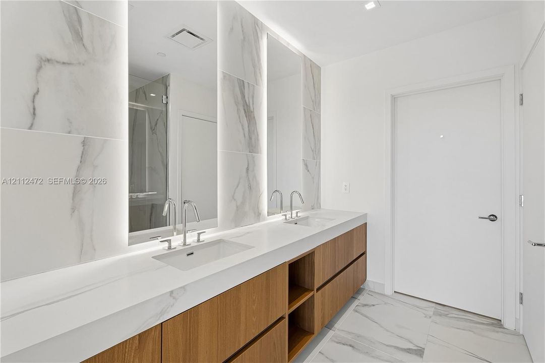 Dual-sink vanity featuring a light-toned solid surface countertop, integrated undermount sinks, and wood-finish cabinetry
