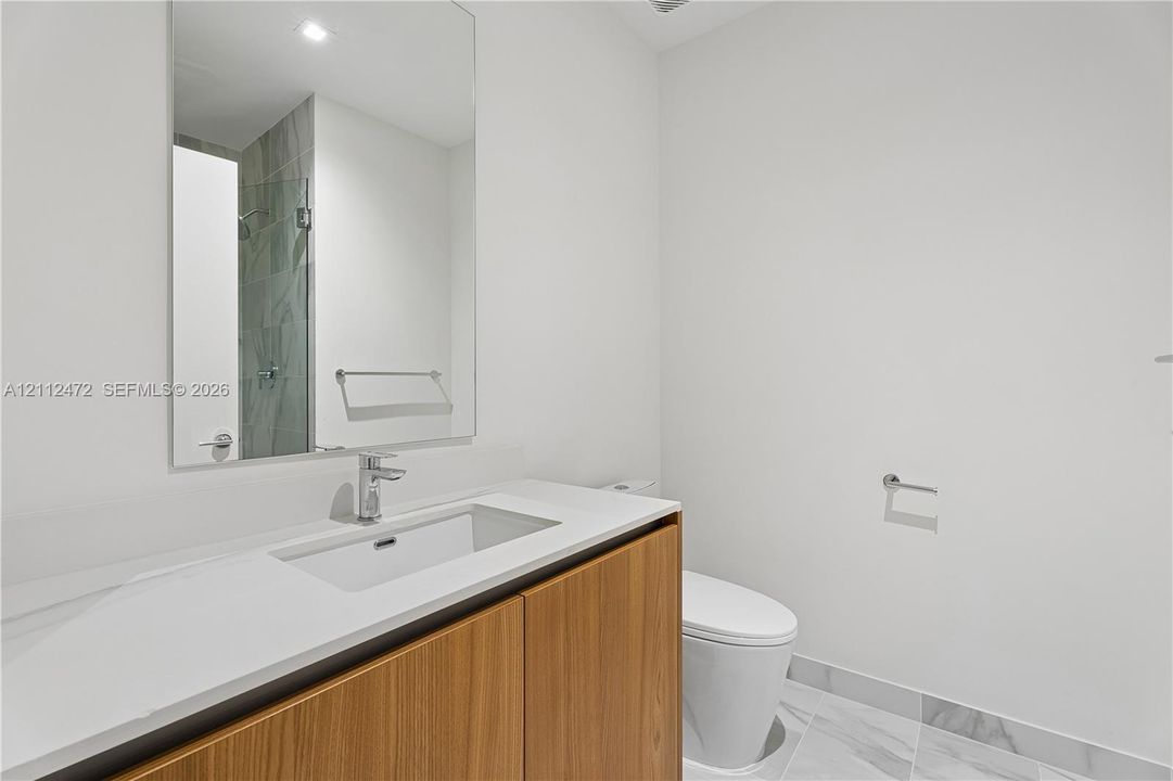Bathroom featuring a vanity with a light-toned wood-finish cabinet and an integrated sink, polished countertop, frameless mirror, and marble-finish tile flooring
