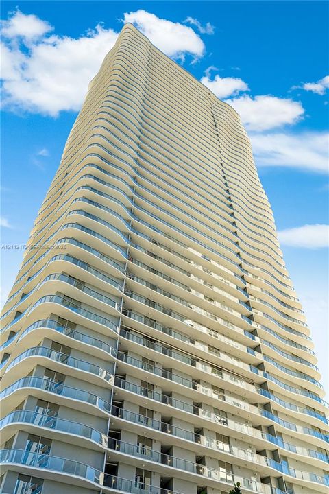 High-rise building featuring a curvilinear architectural design, recessed balconies, glass railings, and expansive exterior windows