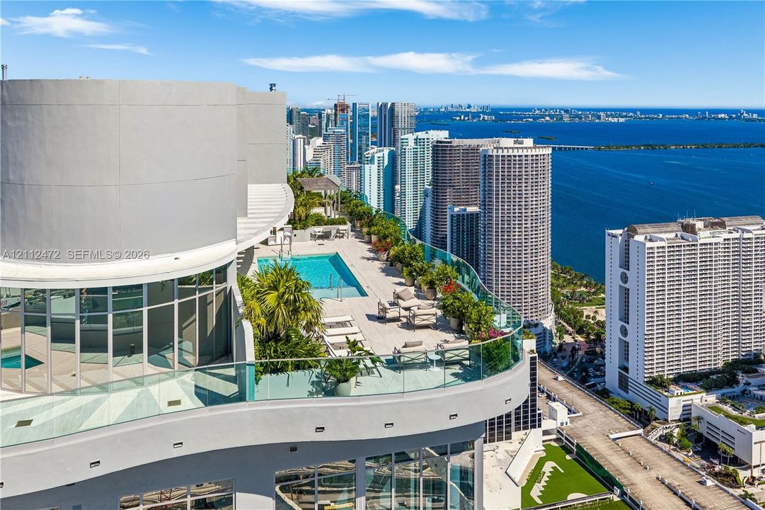 Expansive terrace featuring a rectangular swimming pool, glass paneled perimeter railing, large-format tile flooring, and integrated landscaping