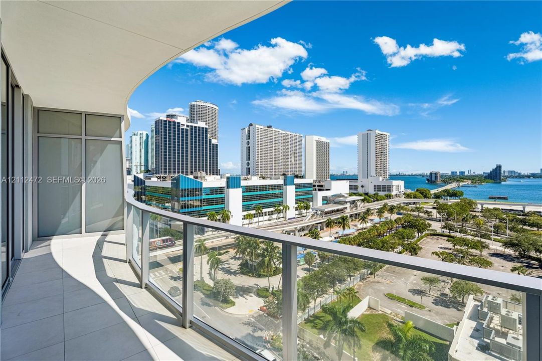 Covered outdoor balcony with tile flooring, glass panel railings, and floor-to-ceiling windows