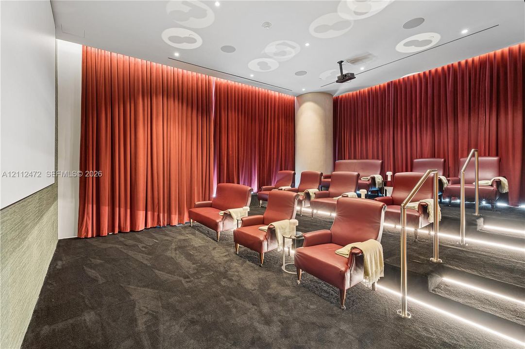 Tiered seating room featuring full-height drapery, recessed ceiling lighting, integrated audio speakers, and illuminated stair lighting