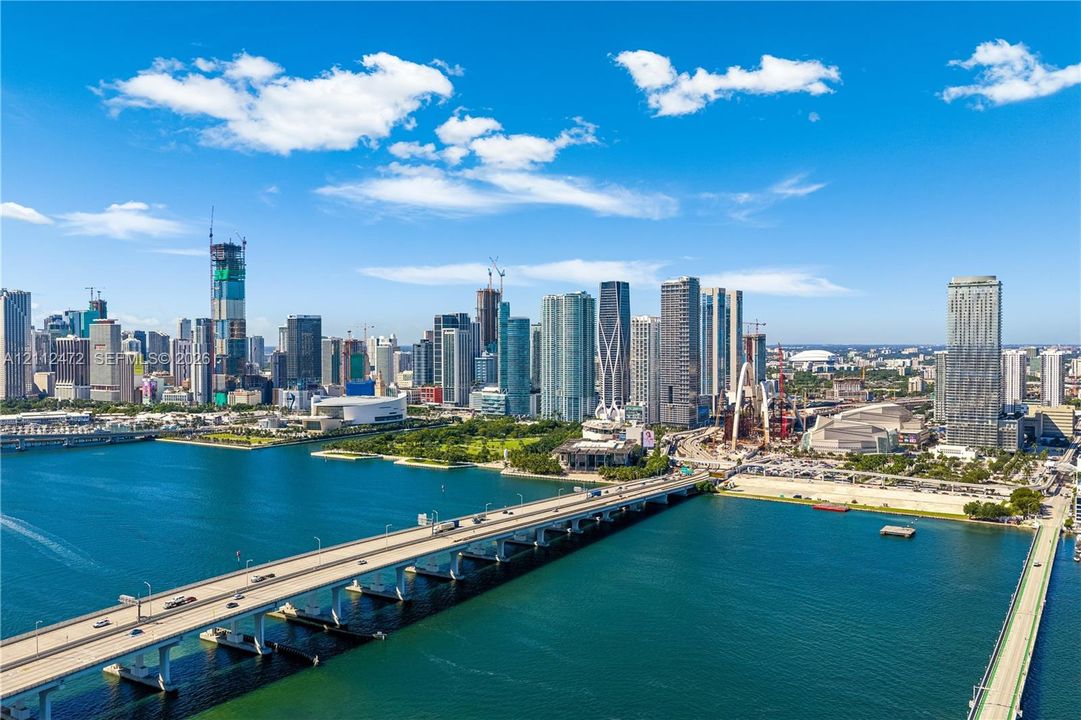 Aerial perspective featuring metropolitan skyline, high-rise architecture, urban waterway, and expansive bridges