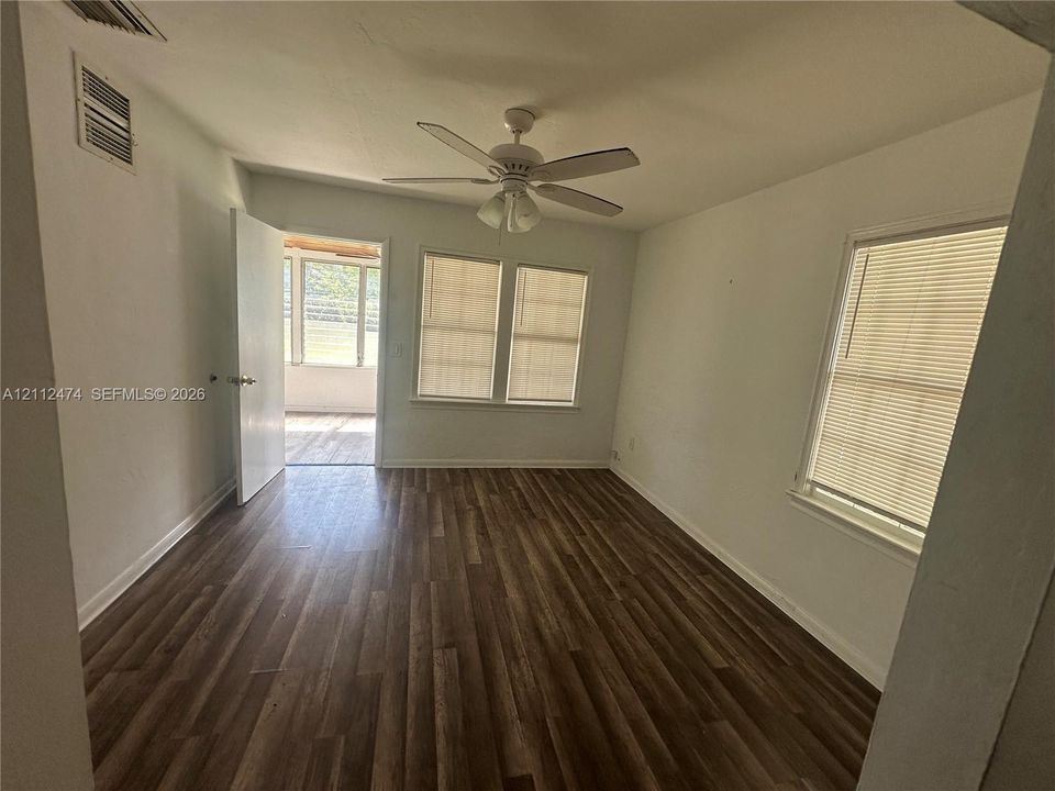 Room featuring wood-finish flooring, a ceiling fan with integrated lighting, and multiple windows with horizontal blinds