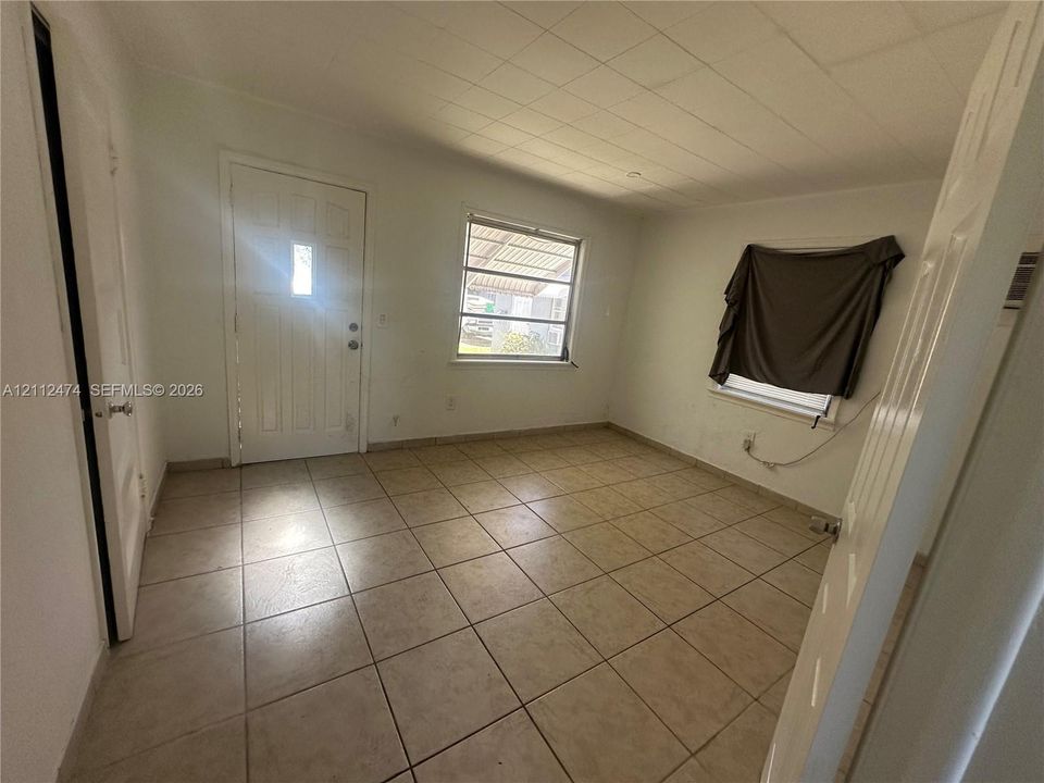 Interior space featuring neutral tile flooring, a multi-pane entry door, dual windows with exterior framing, and a segmented ceiling