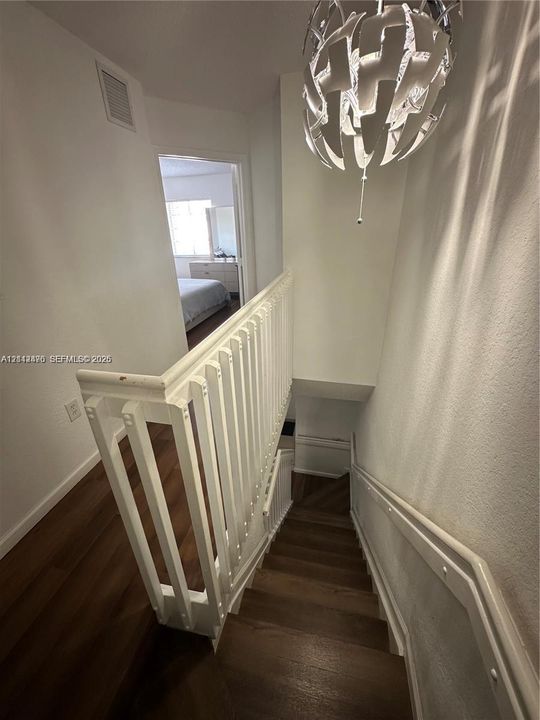 Staircase featuring wood-finish flooring, a white wooden balustrade, and a decorative orb-style pendant light fixture
