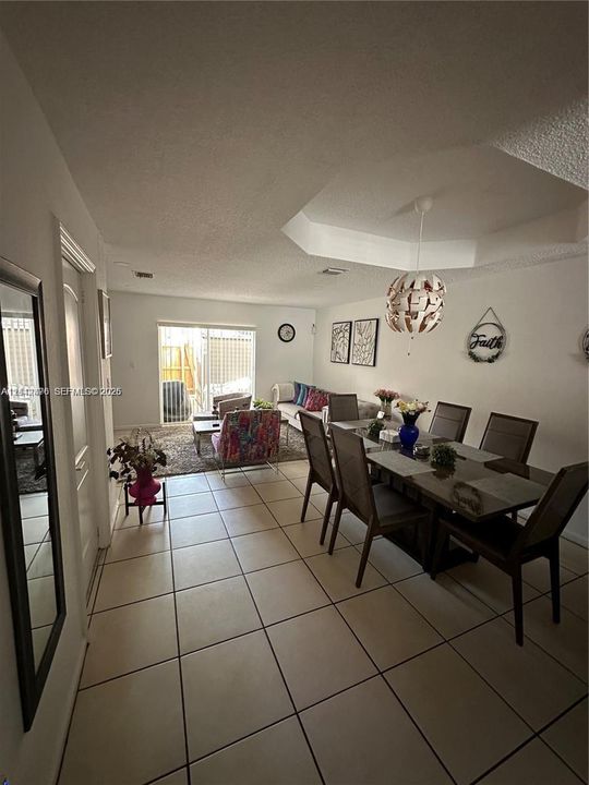 Neutral tile flooring, coffered ceiling with a pendant light fixture, and glass sliding doors leading to the exterior