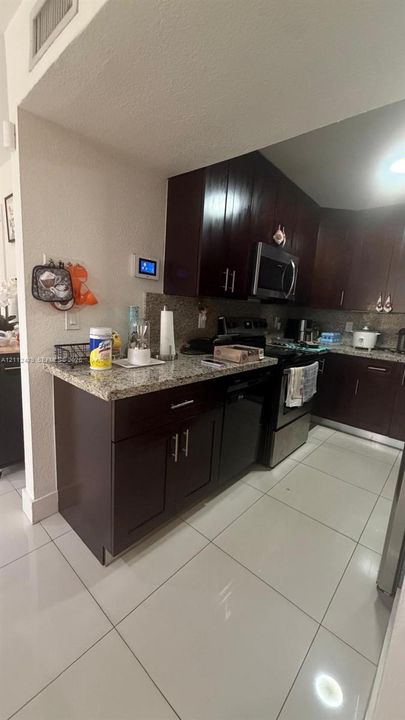 Dark cabinetry featuring brushed nickel hardware, stone-finish countertops, stainless steel appliances, and large-format tile flooring