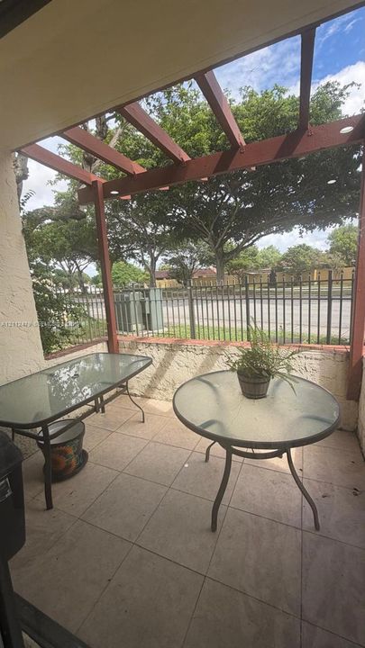 Covered patio featuring a timber-frame pergola, neutral tile flooring, and a low-profile masonry perimeter wall with integrated metal fencing
