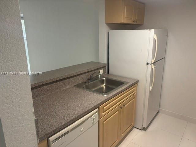 Kitchen area featuring a built-in refrigerator, dishwasher, composite countertop with a stainless steel sink, and wood-finish cabinetry