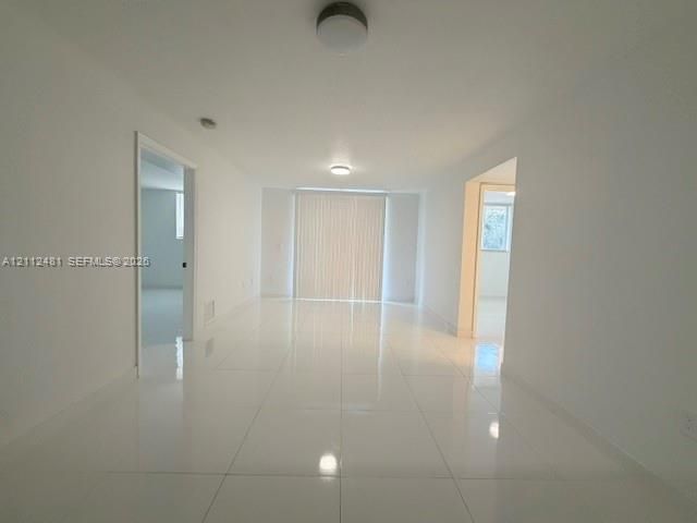 Interior space featuring polished white tile flooring, neutral wall finishes, flush-mount ceiling lighting, and floor-to-ceiling sliding glass doors