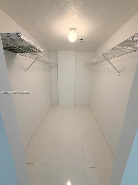 Walk-in storage space featuring ceramic tile flooring, white walls, dual tiered wire shelving, and a central flush-mount ceiling light