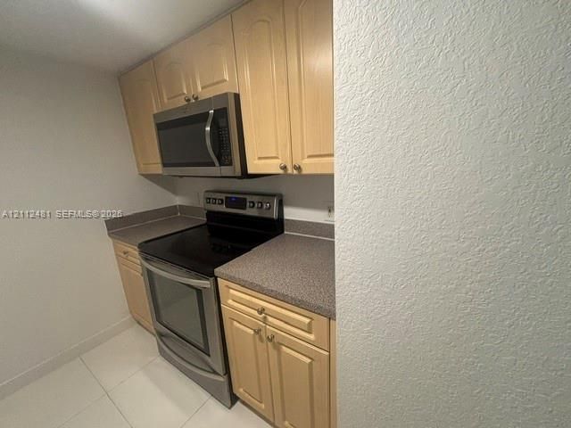 Kitchen featuring light-tone wood cabinetry, solid-surface countertops, and a suite of stainless steel appliances, including an over-the-range microwave and electric range