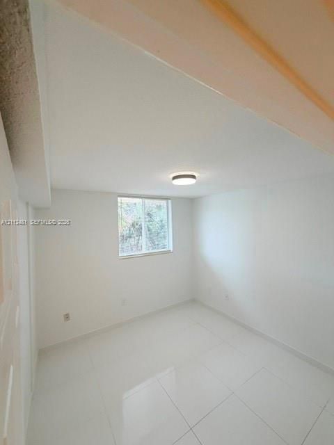 Interior space featuring a vaulted ceiling, glossy tile flooring, a recessed window, and a flush-mount ceiling light