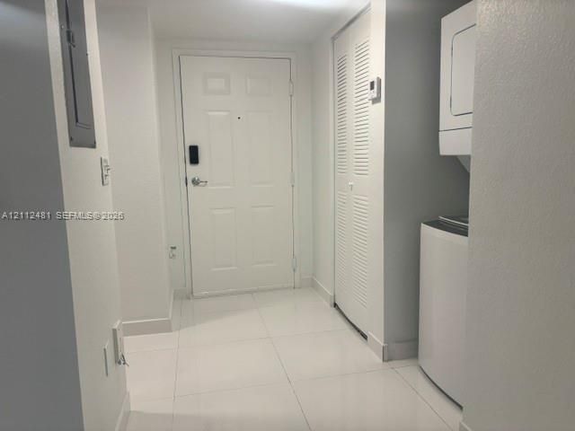 Entryway featuring large-format tile flooring, a six-panel entry door with electronic deadbolt, built-in louvered closet doors, and stacked laundry appliances
