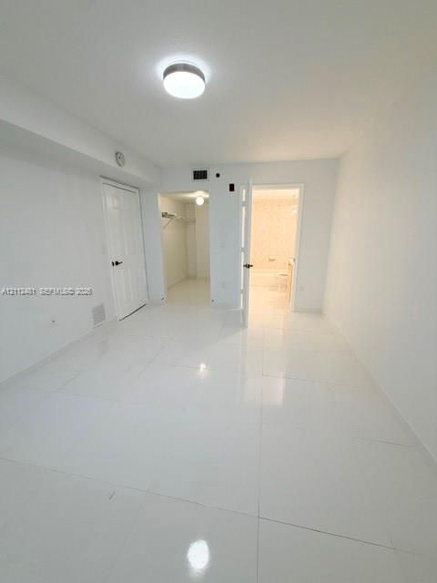 Interior space featuring white tile flooring, flush-mount ceiling lighting, a dedicated walk-in closet with built-in shelving, and an en-suite bathroom