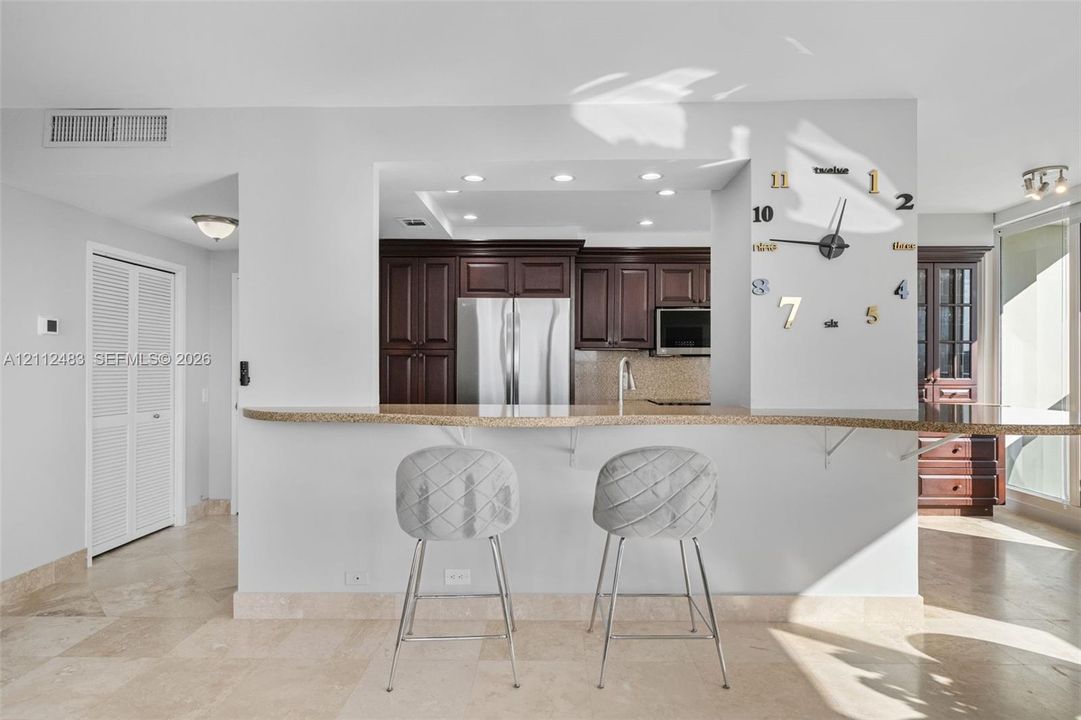 Kitchen pass-through window featuring a stone-topped breakfast bar, dark wood cabinetry, stainless steel appliances, recessed ceiling lighting, and tile flooring