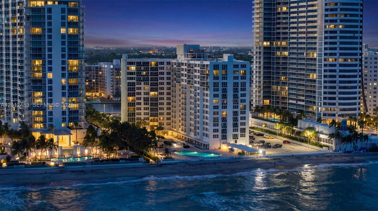 High-rise residential exterior with direct oceanfront access, exterior balconies, and a ground-level swimming pool