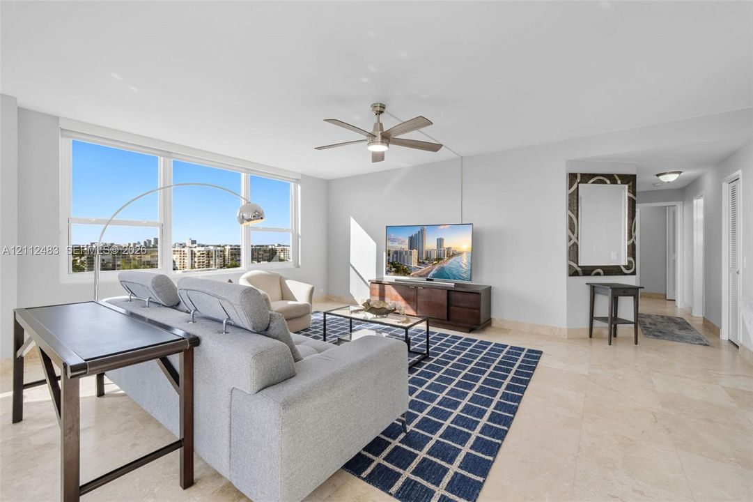 Living area featuring large-format tile flooring, a neutral color palette, a ceiling fan, and expansive windows with exterior scenery