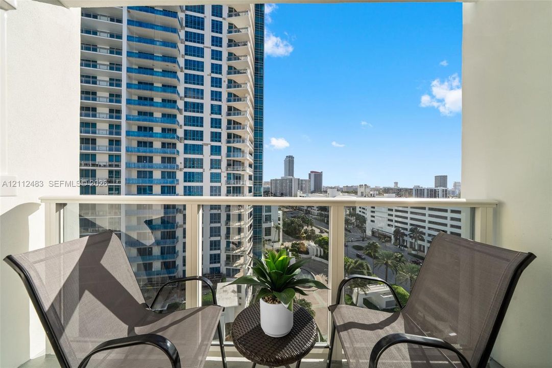 Private balcony featuring a glass panel railing and high-rise urban surroundings