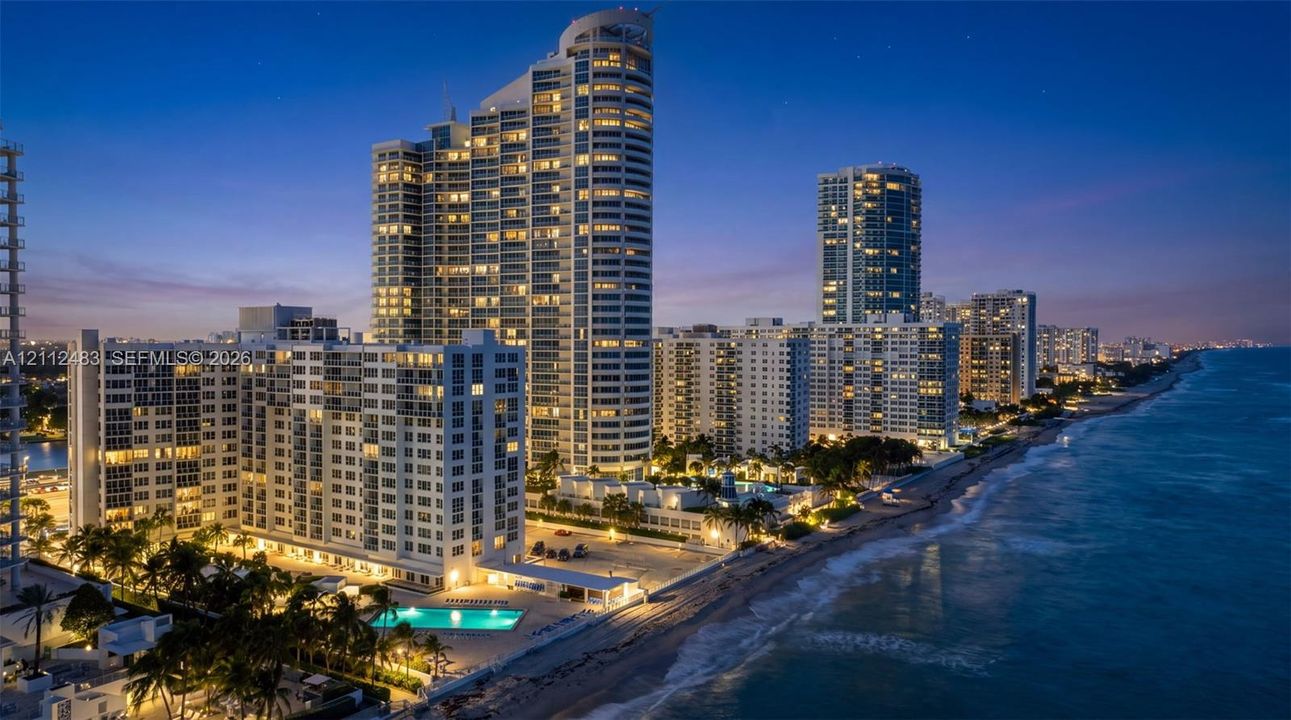 High-rise residential tower featuring glass-facade architecture, direct oceanfront positioning, ground-level swimming pool, and manicured palm tree landscaping