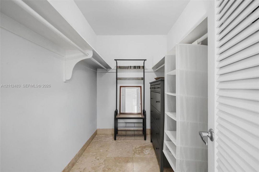 Walk-in closet featuring stone-tiled flooring and extensive built-in shelving with overhead hanging racks