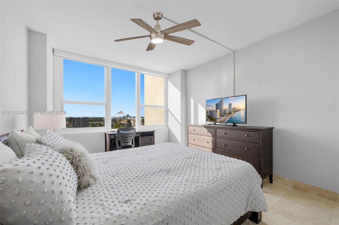 Large floor-to-ceiling windows, natural stone flooring, and a brushed nickel ceiling fan with integrated lighting