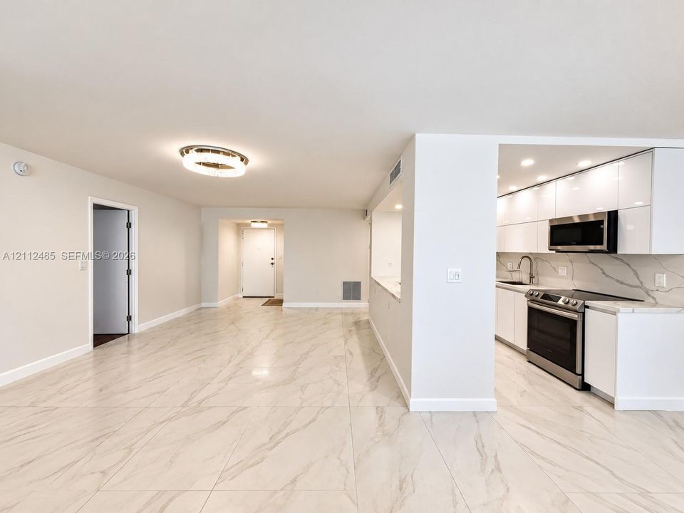 Open-concept floor plan featuring large-format stone-finish flooring, high-gloss white cabinetry, integrated stainless steel appliances, and minimalist ceiling-mounted lighting