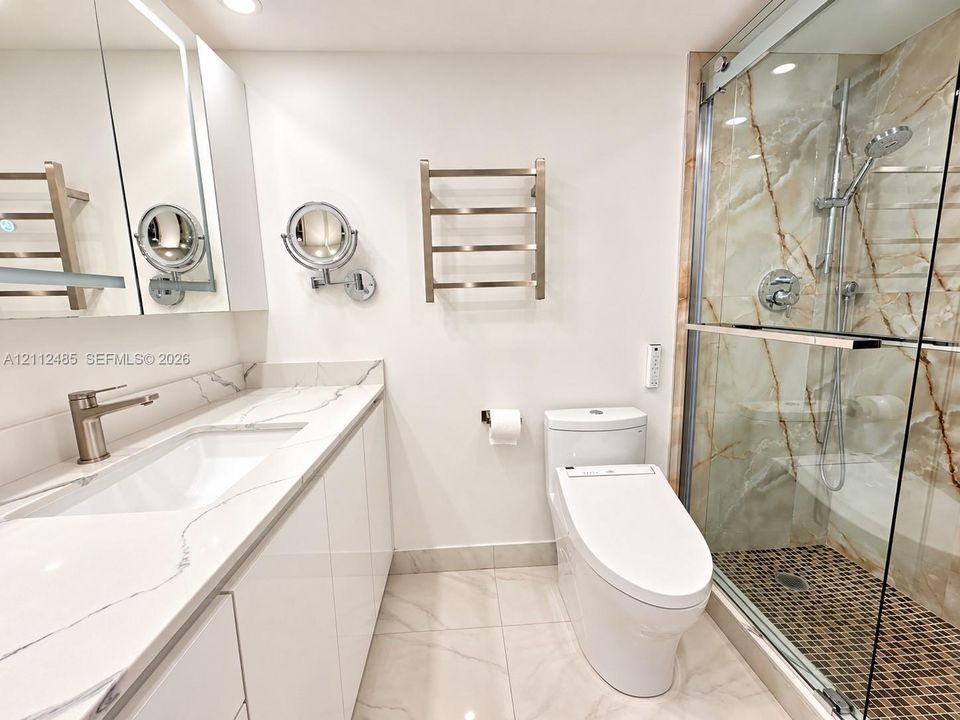 Bathroom featuring a vanity with a white countertop, walk-in shower with glass enclosure and stone-patterned wall tile, wall-mounted heated towel rack, and polished nickel hardware