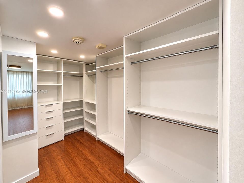 Custom walk-in closet featuring white built-in shelving, integrated dresser drawers, metal hanging rods, and wood-finish flooring