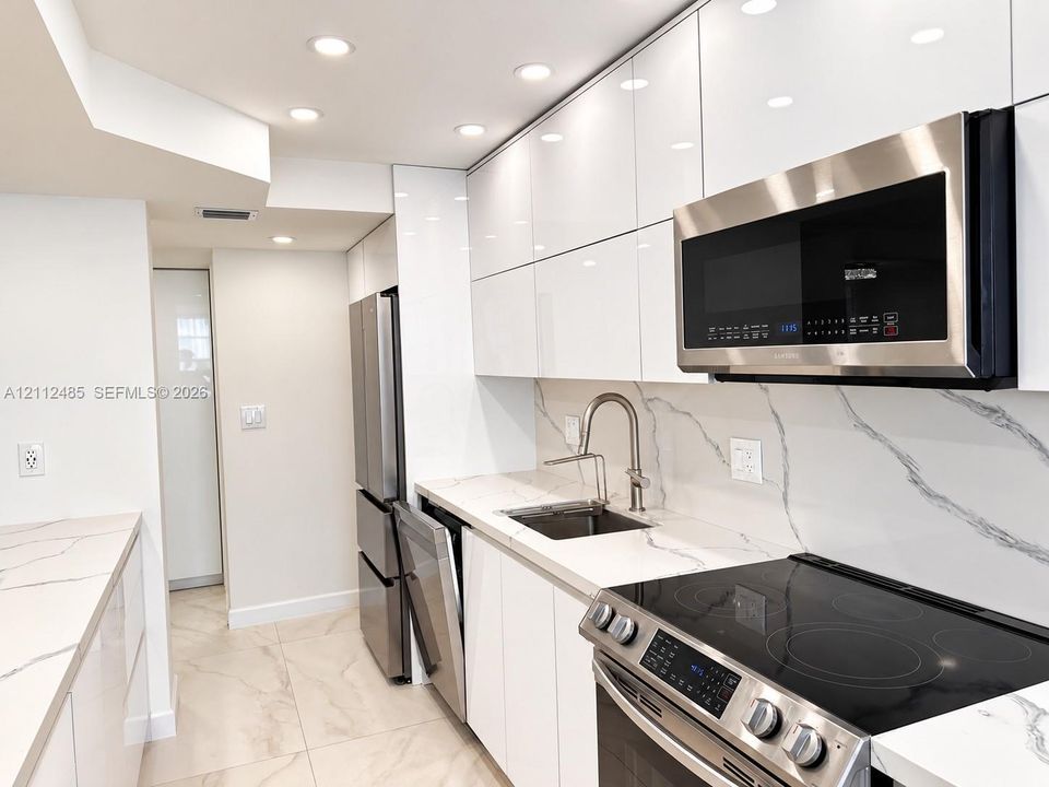 Kitchen featuring high-gloss cabinetry, veined stone-surface countertops, full-height matching backsplash, integrated stainless steel appliances, and recessed ceiling lighting
