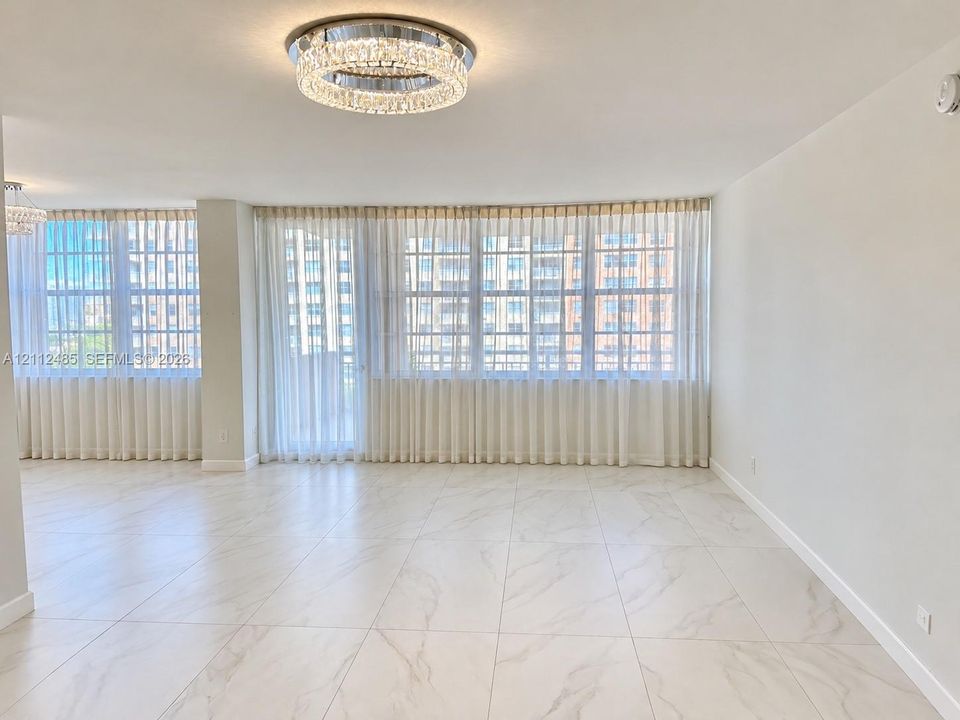Open-concept interior featuring large-format tile flooring with marble-style veining, floor-to-ceiling windows, and a tiered crystal flush-mount ceiling fixture