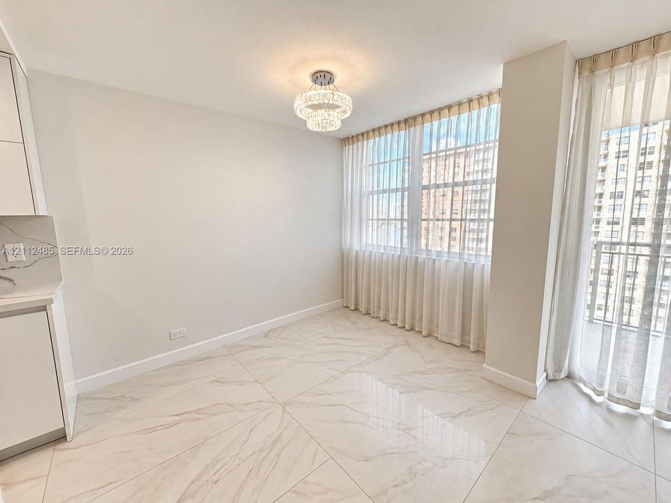 Large-format tile flooring, crystal-accented tiered chandelier, floor-to-ceiling windows, and kitchen cabinetry with quartz-patterned countertops