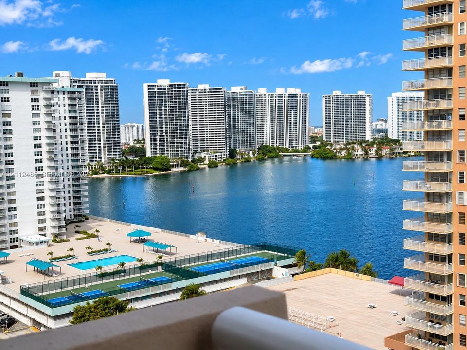 Elevated balcony overview featuring an outdoor swimming pool, fenced tennis courts, and expansive water frontage