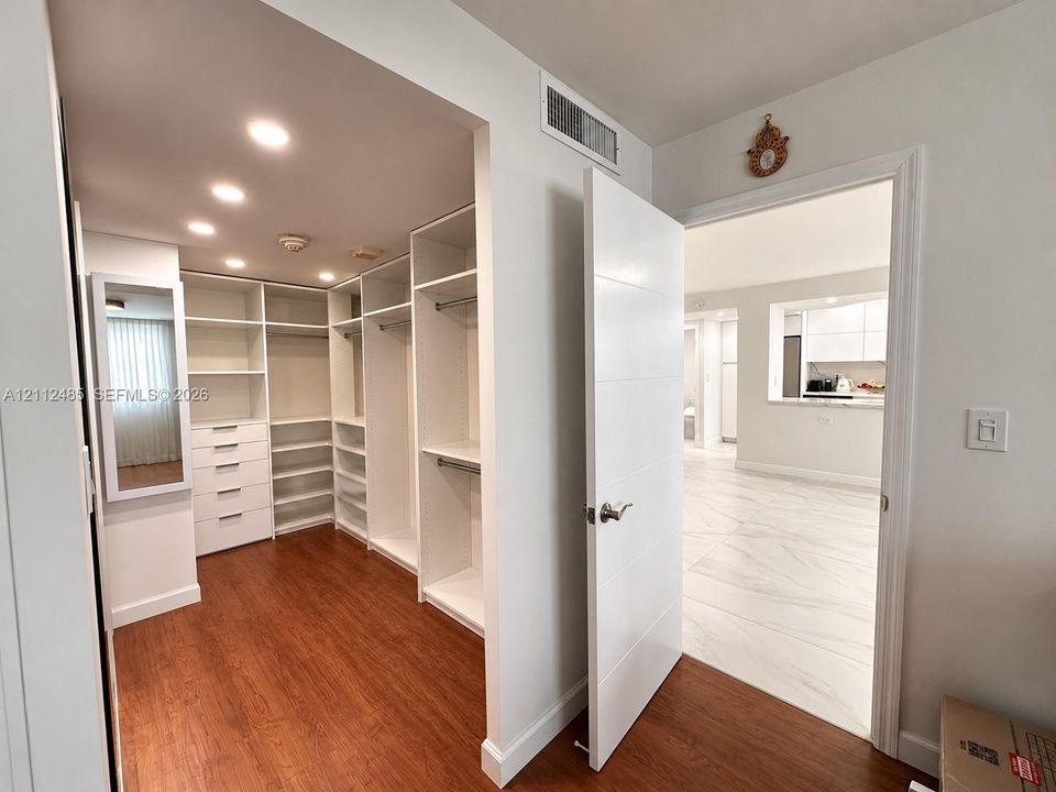 Custom walk-in closet featuring white built-in shelving, integrated dresser drawers, recessed lighting, and wood-finish flooring