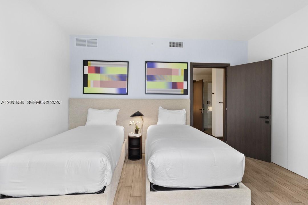 Neutral-toned upholstered headboard with integrated nightstand, wood-finish flooring, and dark-finished solid core swing door
