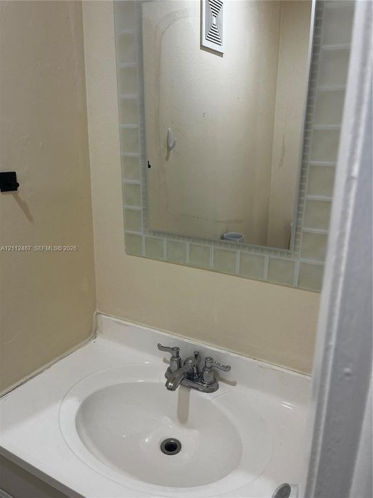 White vanity with an integrated sink basin and double-handle chrome faucet, accompanied by a wall-mounted mirror framed with square glass tile detailing