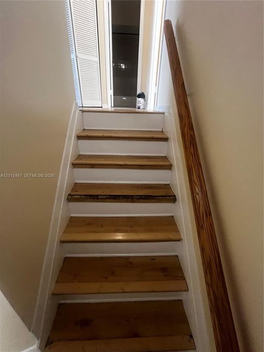 Staircase featuring natural wood treads, white risers, and a mounted wood handrail