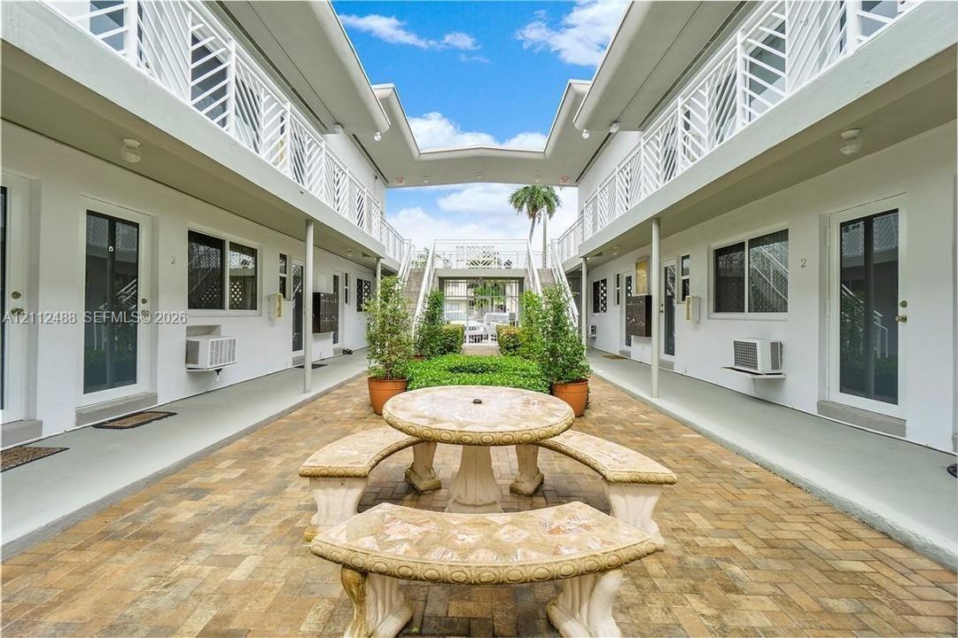 Courtyard area featuring brick paver flooring, stone masonry seating, metal lattice railings, and exterior walkways
