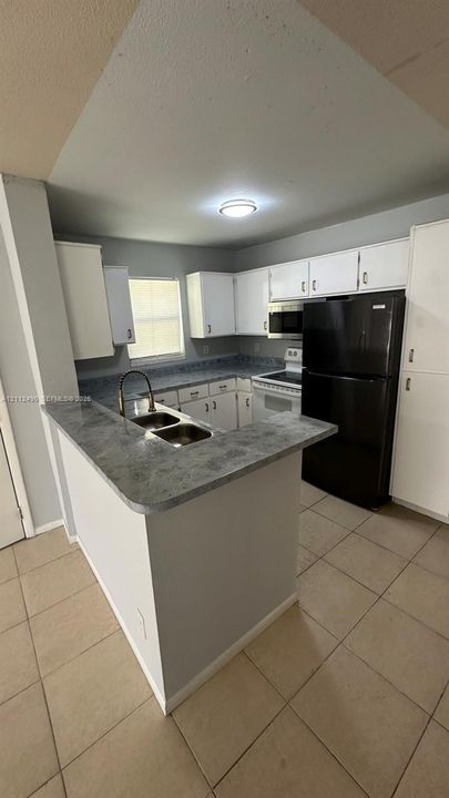 Kitchen featuring white cabinetry, solid-surface countertops, dual-basin stainless steel sink, tiled flooring, and built-in appliances