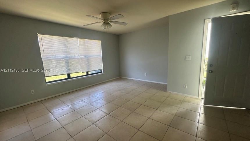 Neutral-toned interior featuring large-format tile flooring, a ceiling fan with integrated lighting, and a window with horizontal blinds