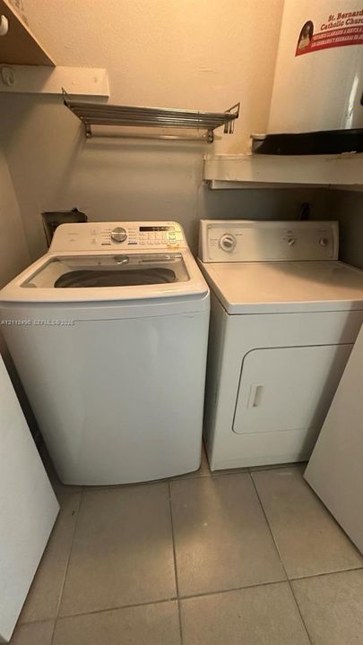 Utility area featuring white tile flooring, built-in wall shelving, and a wall-mounted metal rack