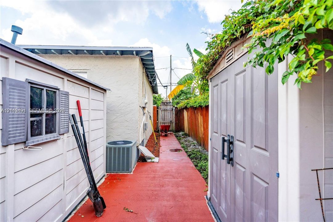 Side exterior area featuring a paved walkway, two storage structures, and perimeter wood fencing